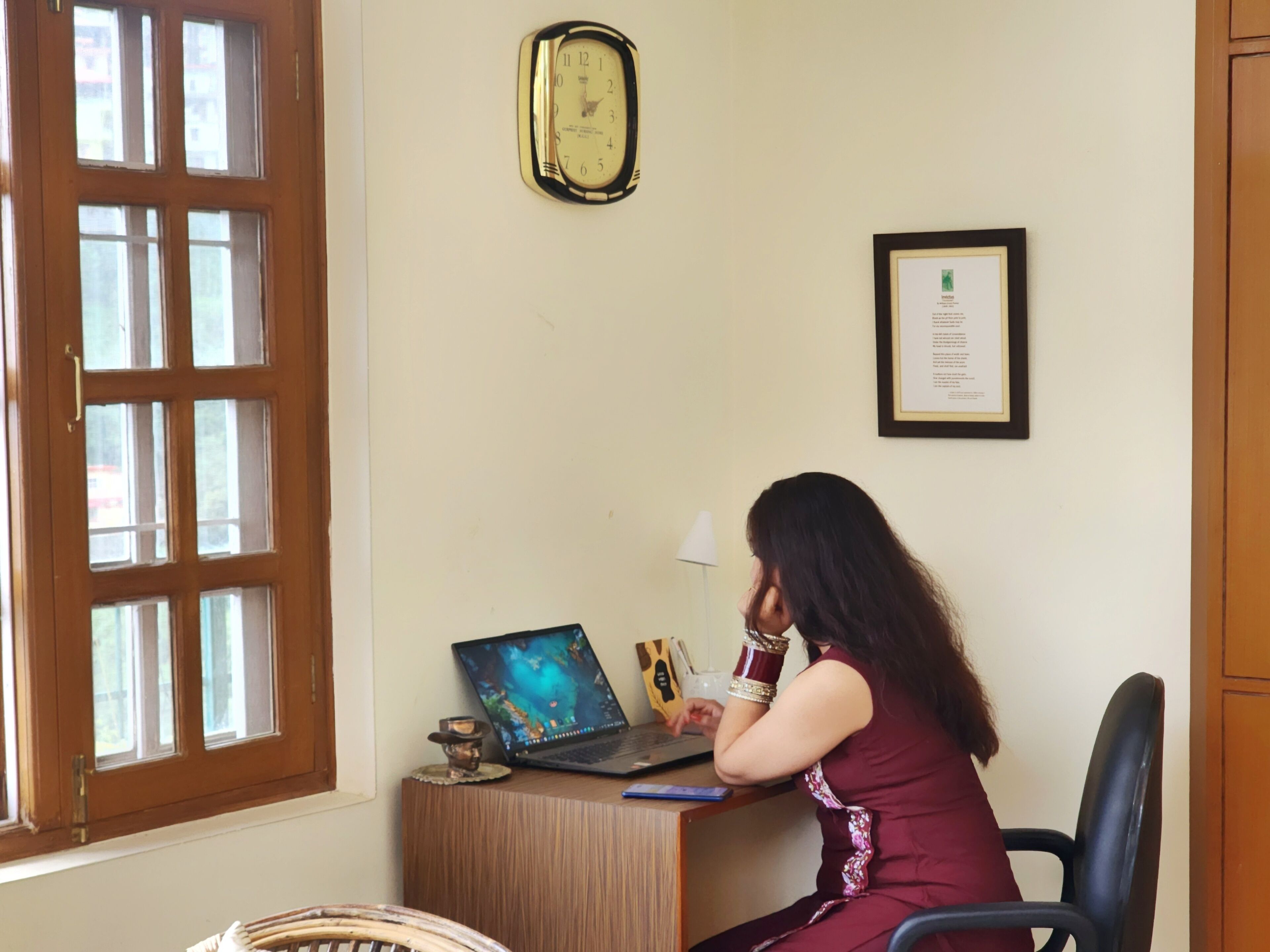 Quarto com escrivaninha de madeira, um laptop, um certificado emoldurado e um relógio de parede.