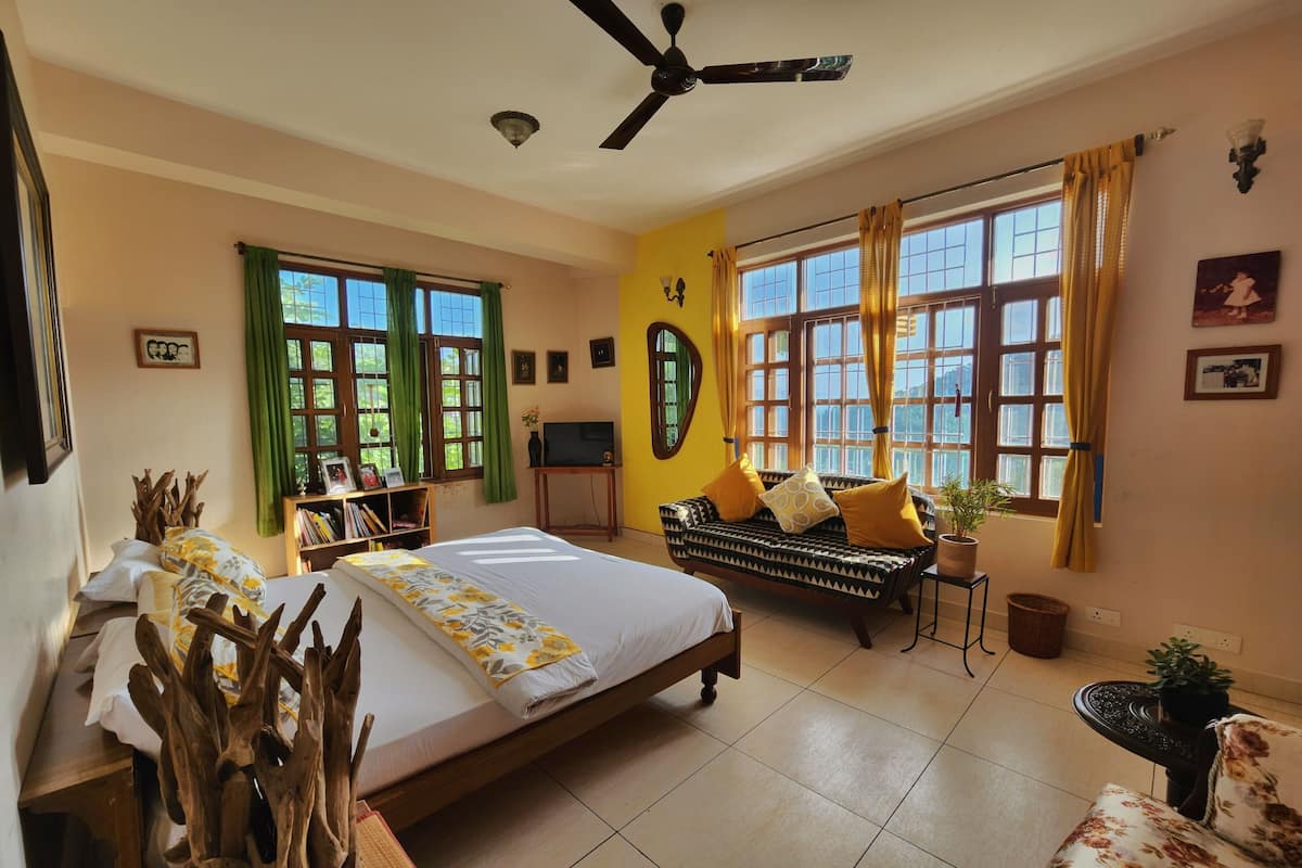 A bedroom with a bed, a sofa, a ceiling fan, and large windows with curtains.