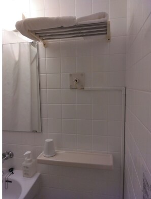 A bathroom with white tiles, a towel rack, a shelf with toiletries, and a mirror.