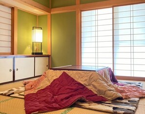 A traditional Japanese-style room with tatami flooring, a futon bed, a shoji screen, and a low wooden table with a lamp.