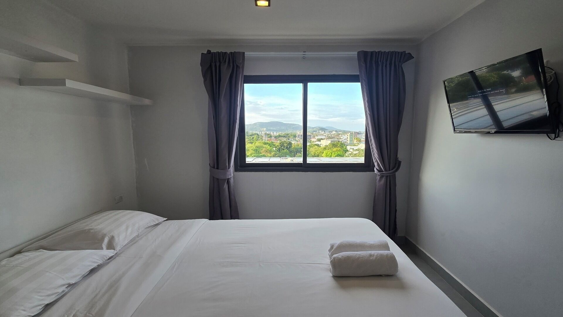 A hotel room with a bed, a TV mounted on the wall, and a window with curtains.