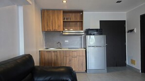 Cocina compacta con armarios de madera, refrigerador de acero inoxidable y microondas.
