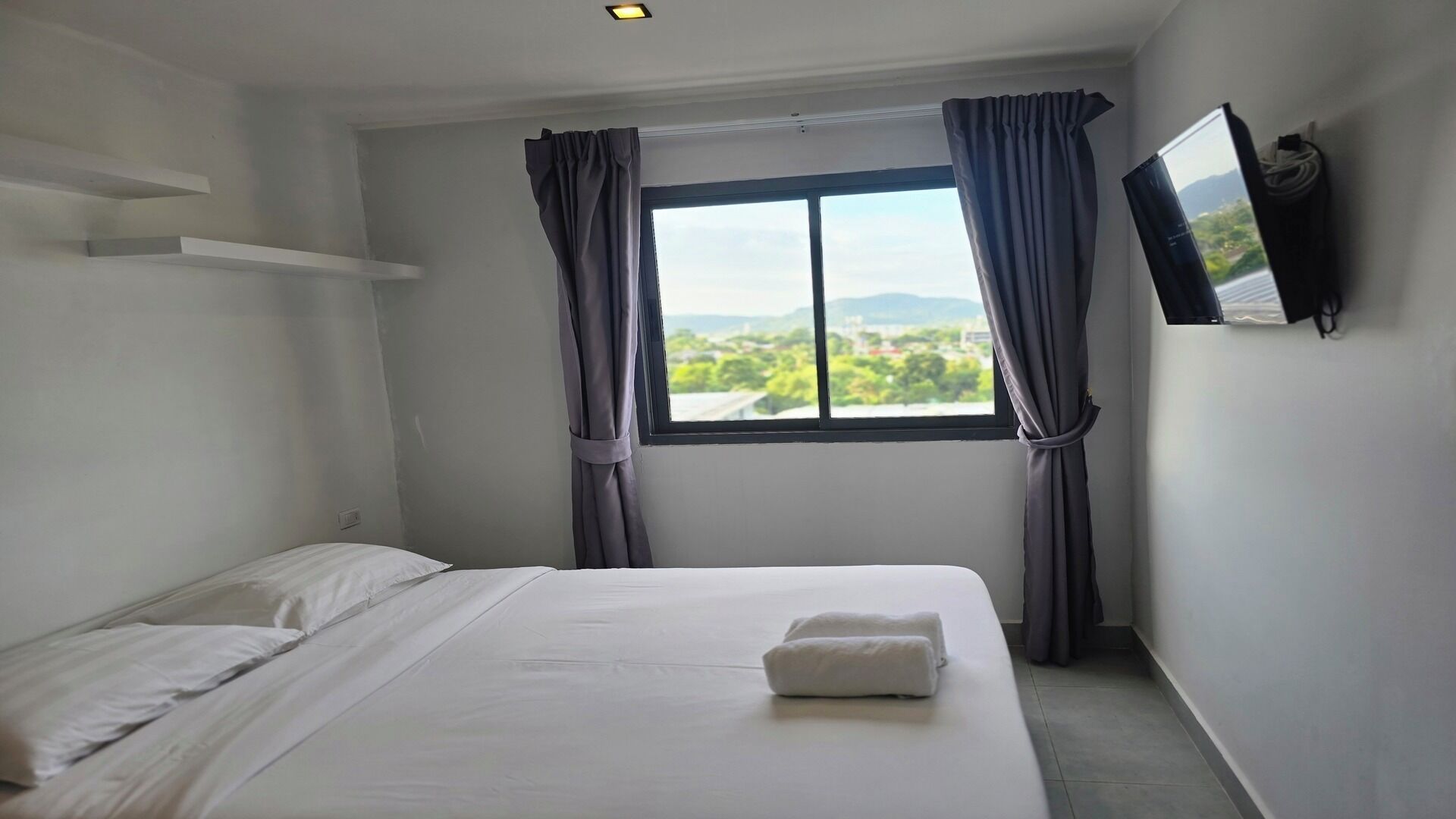 Ein Hotelzimmer mit Bett, einem fenster mit Vorhängen, einem an der Wand befestigten Flachbildfernseher und Blick auf Grünflächen.