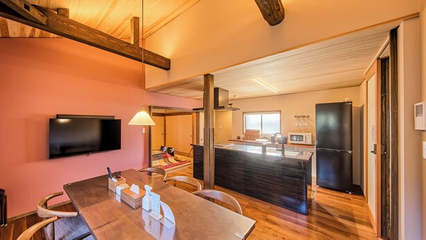 Una cocina moderna con una isla grande, un televisor de pantalla plana montado en la pared y una zona de comedor con una mesa y sillas de madera.