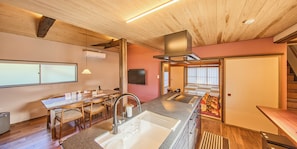 A modern kitchen with a central island, wooden dining table, and chairs, a built-in stove, and a large window.