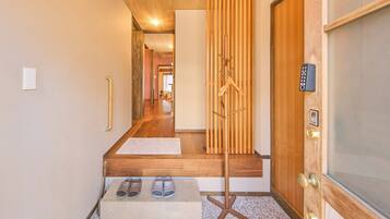 A hallway with a wooden floor, a coat rack, a door with a keypad, and a small table with shoes.