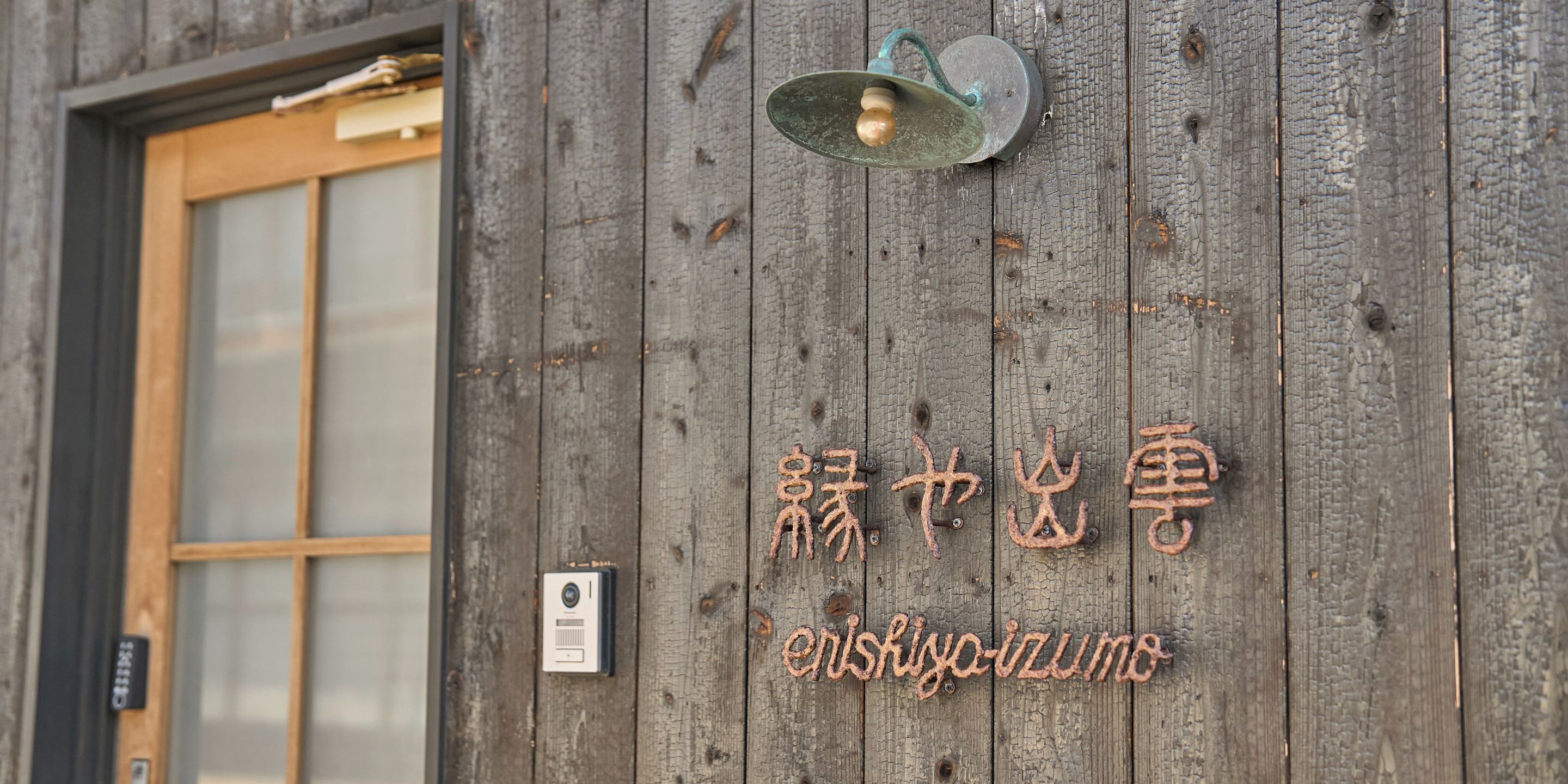A rustic wooden wall with a metal light fixture and a security camera.