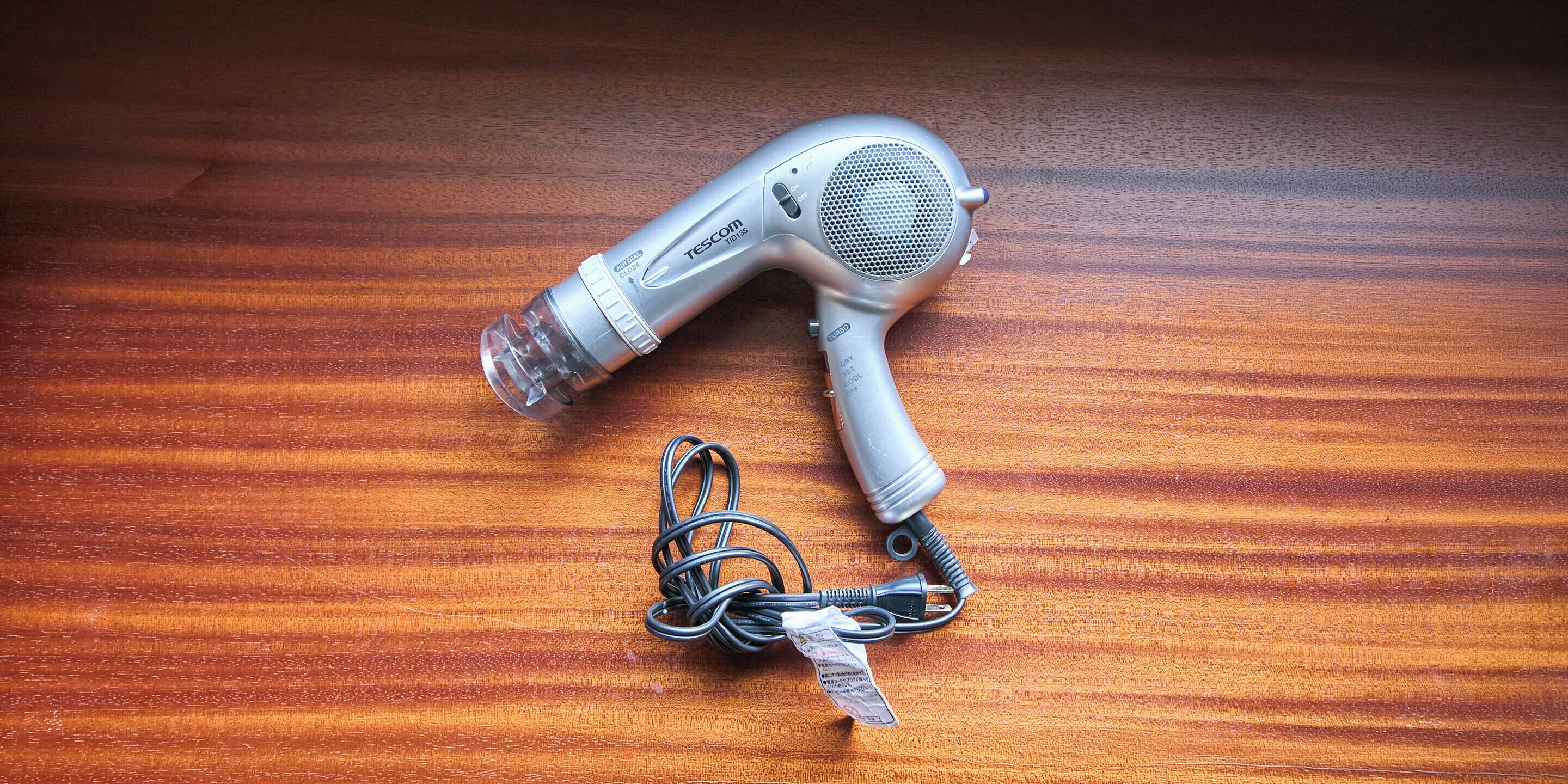 Un secador de pelo con cable y un adaptador de corriente sobre una superficie de madera.