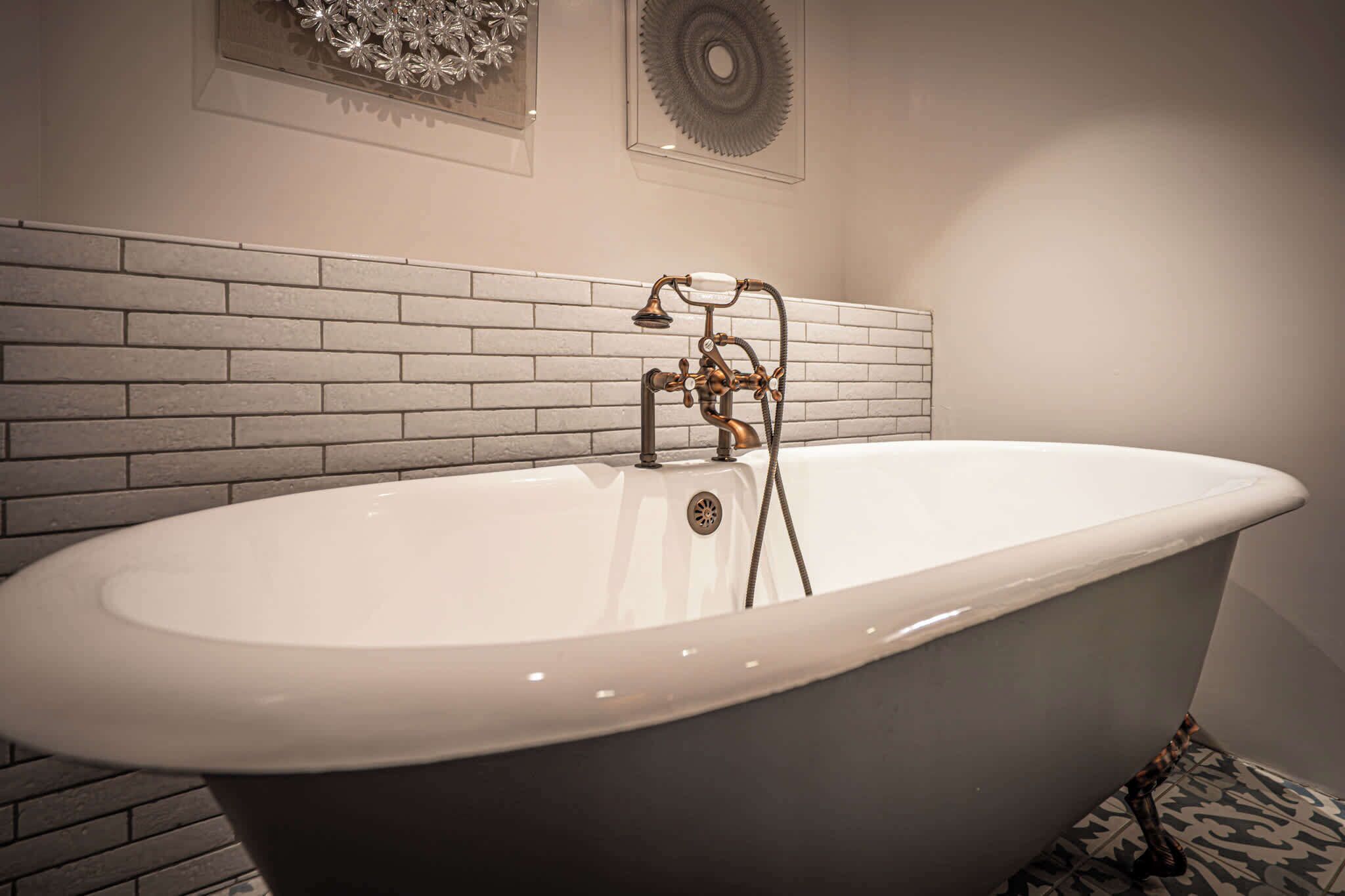 A freestanding bathtub with a vintage design, a tiled wall, and a decorative wall piece above it.