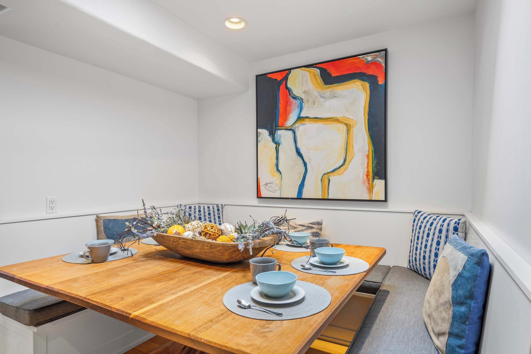 Un coin repas avec une table en bois, des bols bleus et un grand tableau abstrait accroché au mur.