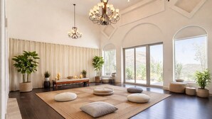 Amplia habitación con alfombra grande, zona de estar, plantas en macetas y vistas a través de amplias ventanas.
