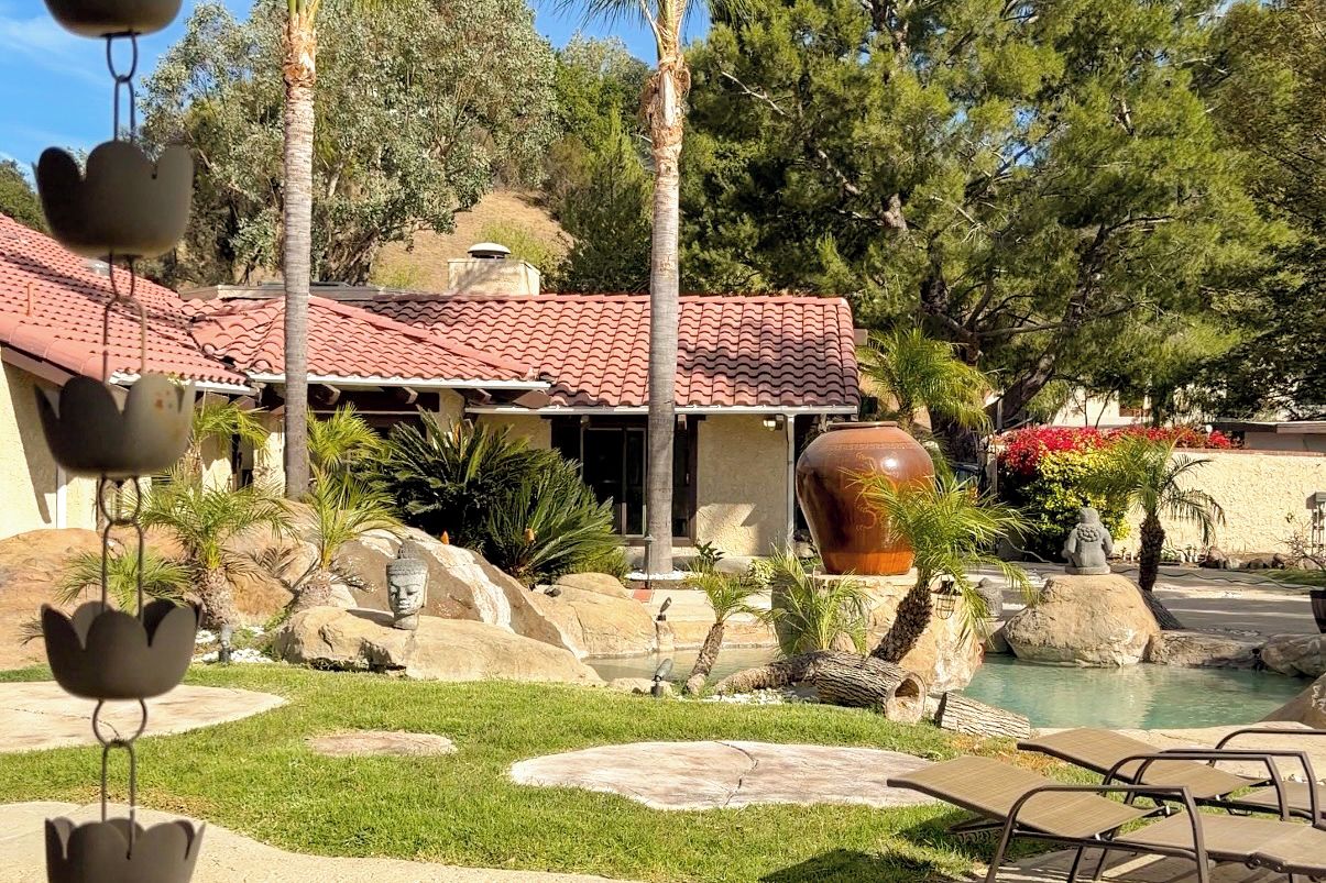 A pool area with lounge chairs, a large decorative vase, and a building with a red-tiled roof.