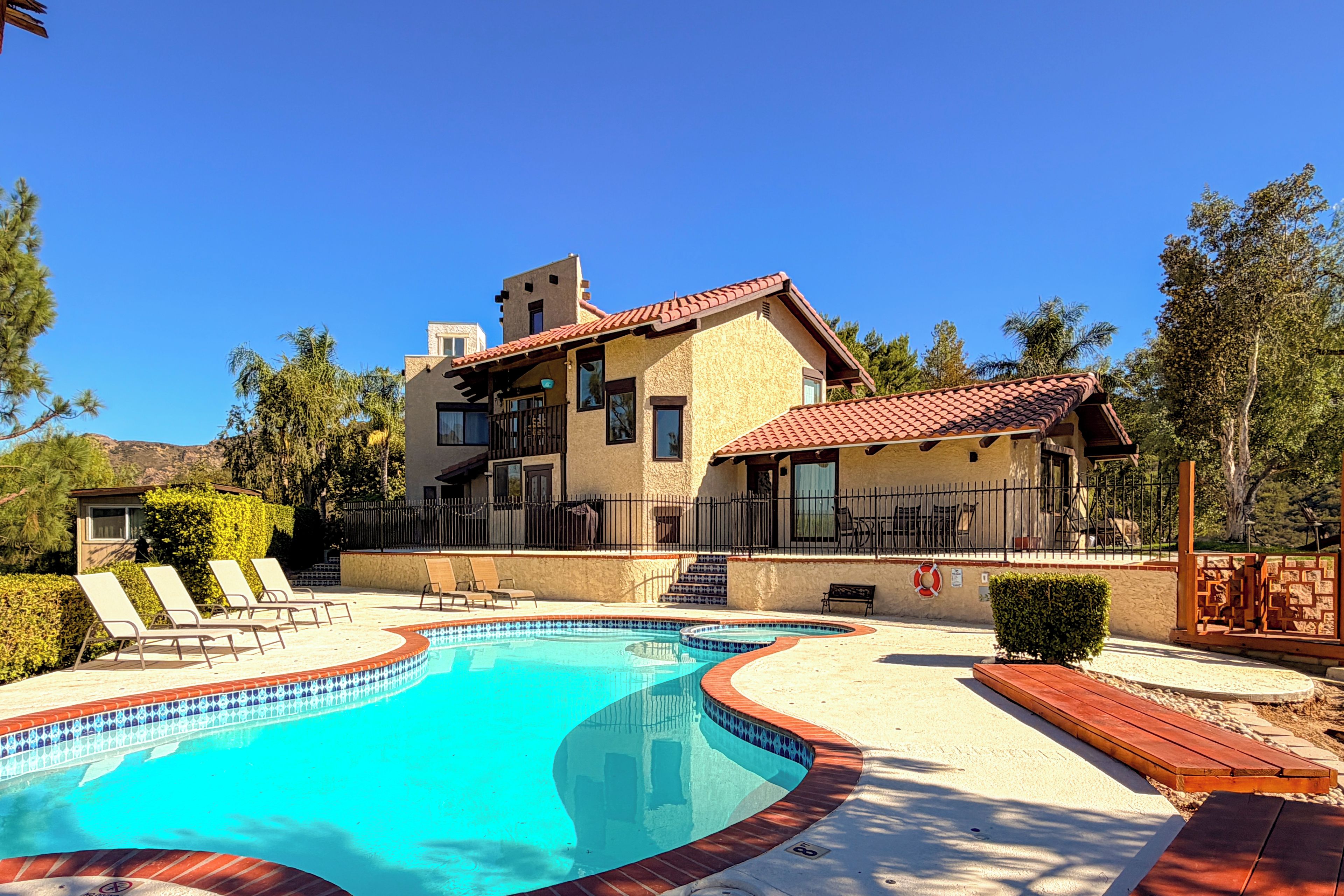 Una casa de dos pisos con piscina, un patio con sillones de descanso y vistas del paisaje circundante.