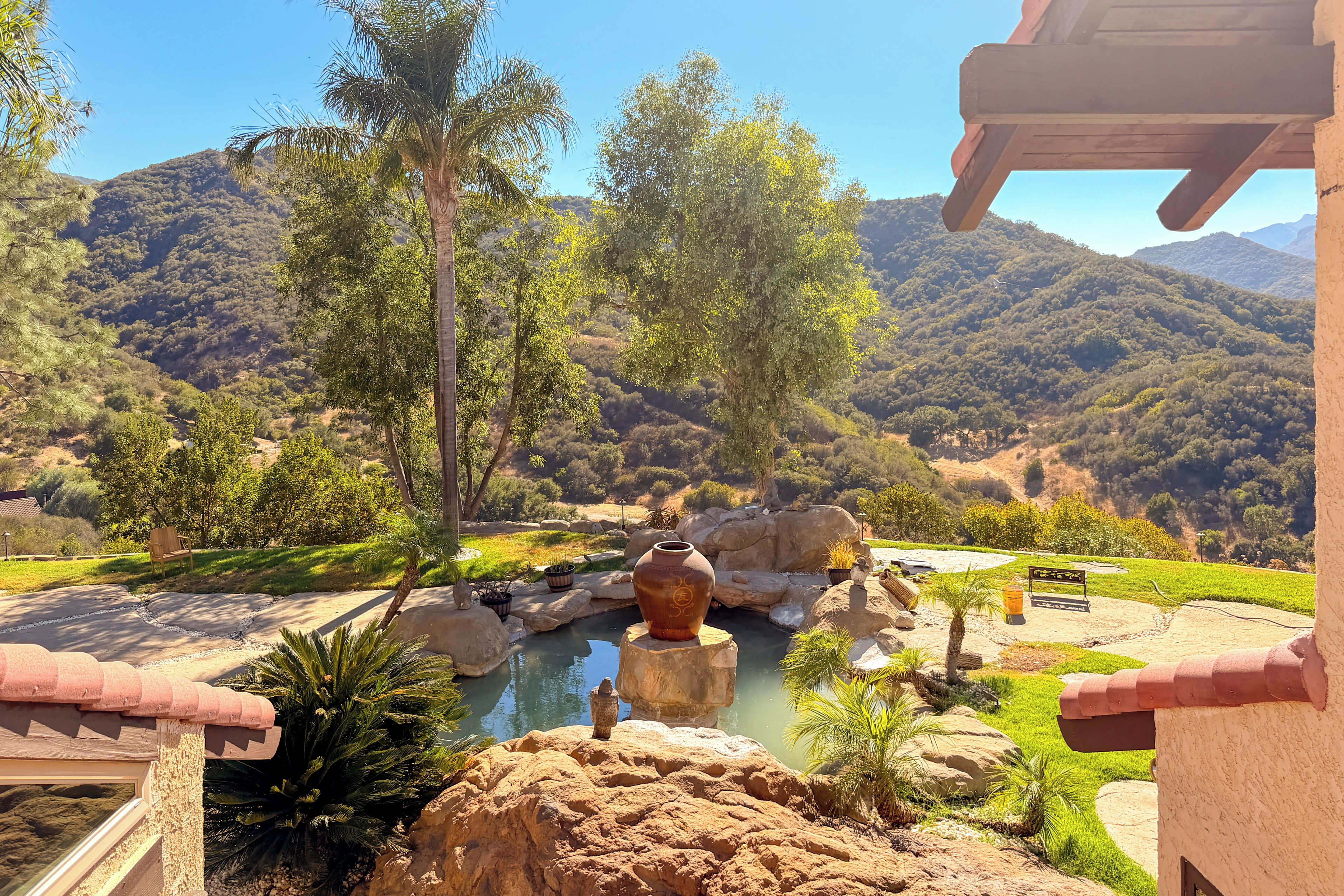 Ein angelegter Garten mit Wasserspiel, Bänken und Blick auf eine gebirgige Landschaft.