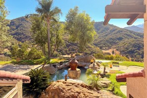 Ein angelegter Garten mit Wasserspiel, Bänken und Blick auf eine gebirgige Landschaft.