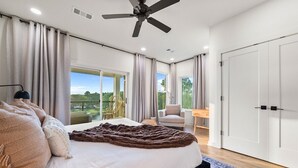A bedroom with a bed, a ceiling fan, a view through a large window, and a door to another room. - Side-by-Side Lake Hamilton Homes w/Dock, Pool (Hot Springs)