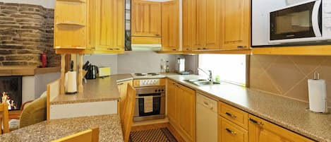 Cozinha com armários de madeira, micro-ondas, fogão e área de refeições com uma cadeira e mesa.