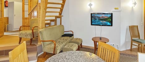 Un intérieur chaleureux avec un escalier en bois, un téléviseur à écran plat fixé au mur et un coin repas doté d’une table en granit.
