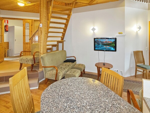 A cozy interior with a wooden staircase, a flat-screen TV mounted on the wall, and a dining area with a granite table.