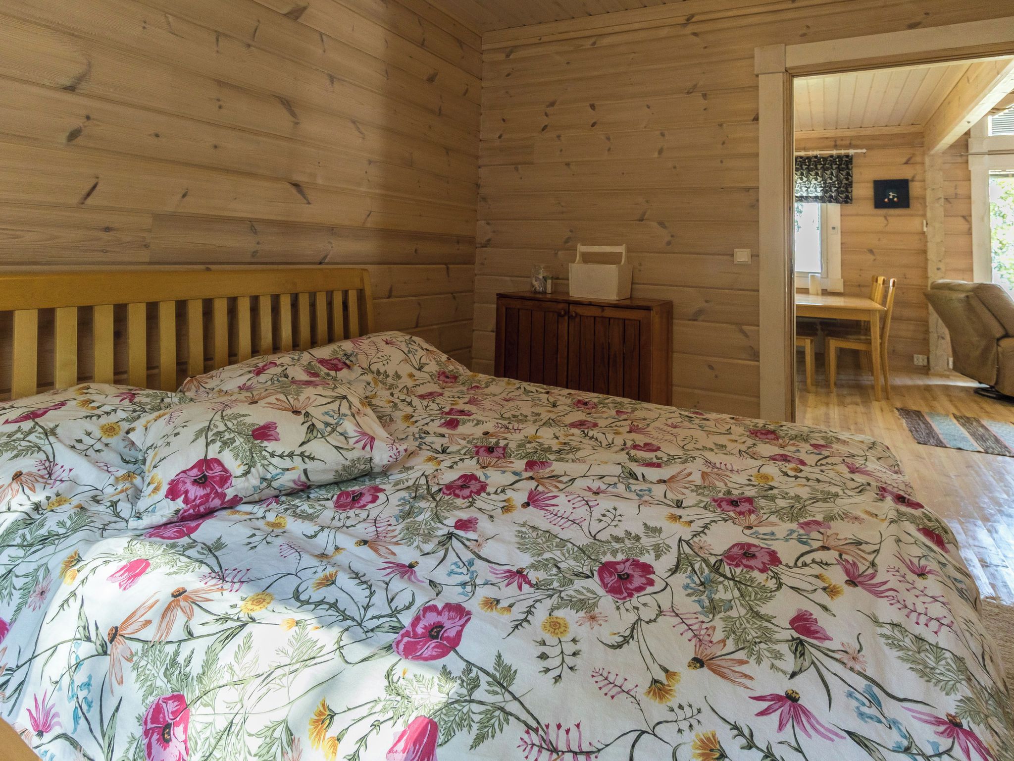 A wooden cabin interior with a bed, a small table, and a dining area.