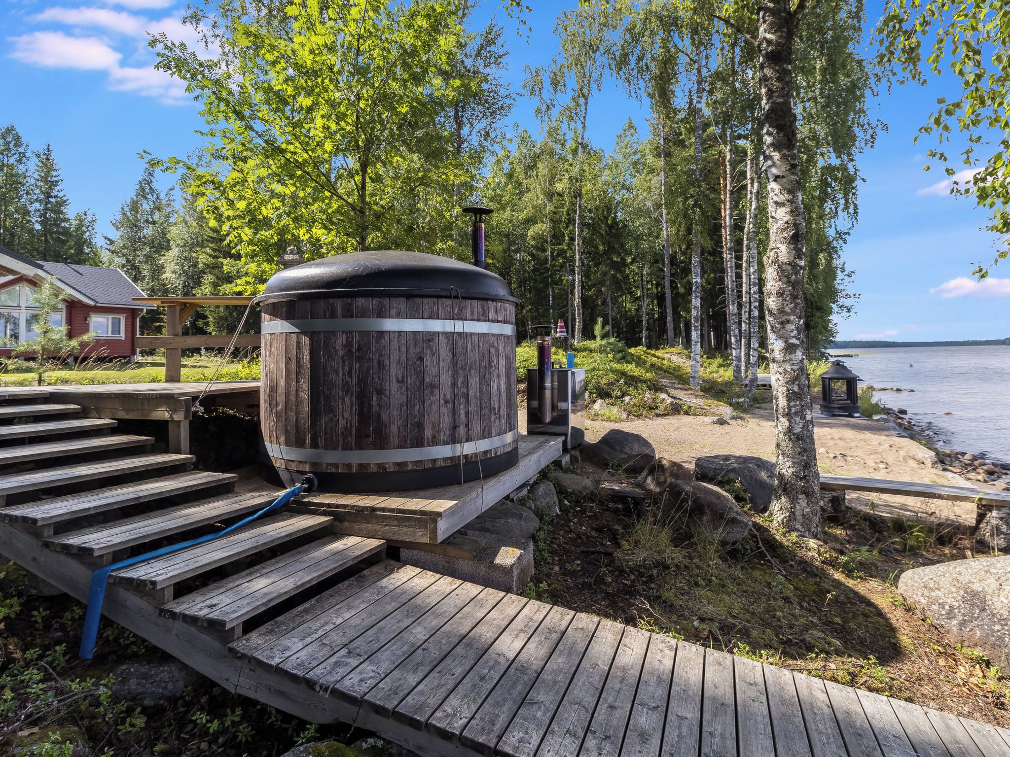 A wooden deck leading to a large cylindrical water heater, surrounded by a natural landscape with trees and a body of water.