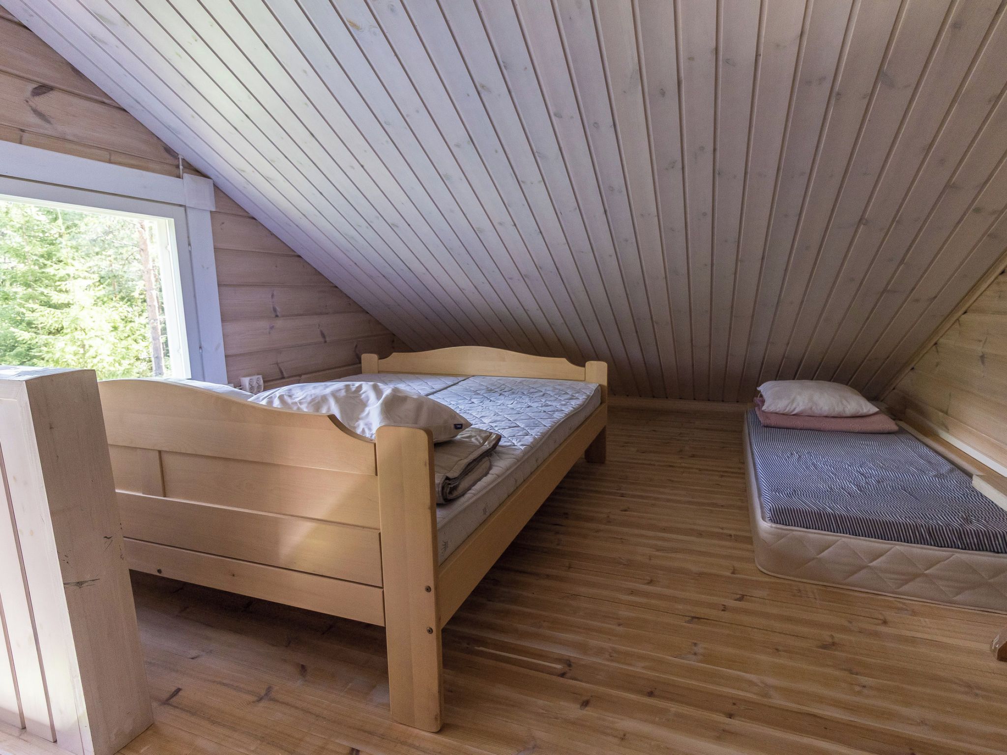 A small, wooden room with two beds, one larger and one smaller, and a window providing natural light.
