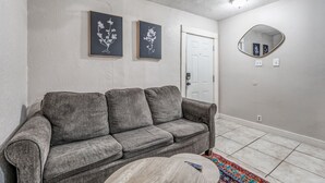 A living room with a gray sofa, two framed floral wall art pieces, a round mirror, and a door. - Cozy Central Hideaway in Midtown Memphis (Memphis)