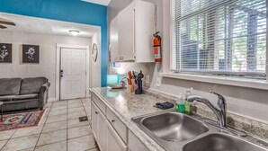 A kitchen with a double sink, white cabinets, a blue accent wall, and a window with blinds. - Cozy Central Hideaway in Midtown Memphis (Memphis)