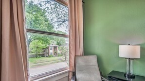 Une pièce avec vue sur une maison, visible à travers une fenêtre, comprenant une chaise, une lampe et un mur vert.