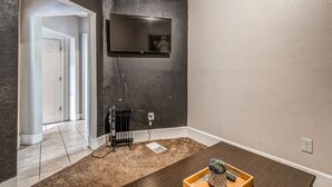 Une pièce avec un mur d’accent de couleur foncée, un téléviseur fixé au mur, un radiateur et une table en bois sur laquelle se trouve un plateau.