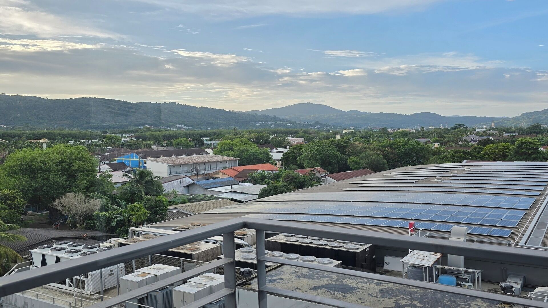 A rooftop with solar panels, air conditioning units, and a view of a town with buildings and mountains in the distance.