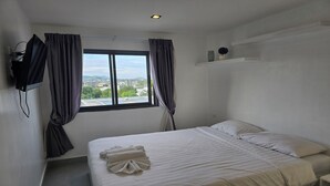 A hotel room with a bed, a TV mounted on the wall, a window with curtains, and a view of the cityscape. - Urban loft 1BR T1-706 (Chalong)