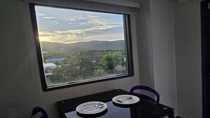 A dining area with a table set for two, a window with a view of a valley and mountains, and a purple chair. - Urban loft 1BR T1-706 (Chalong)