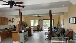 Una cocina amplia con una isla central, un comedor con sofá y sillas, y una sala de estar con un ventanal grande.