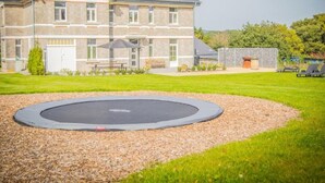 A building with a stone facade, a grassy lawn, and a trampoline in the foreground. - Mansion with sauna and spacious garden (Durbuy)