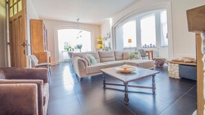 A spacious living room with a large sofa, a coffee table, and a dining area visible through an open door. - Mansion with sauna and spacious garden (Durbuy)