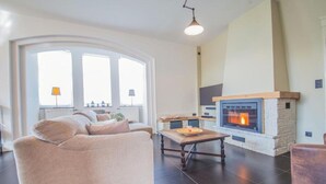 A living room with a sofa, a fireplace, and a dining table. - Mansion with sauna and spacious garden (Durbuy)