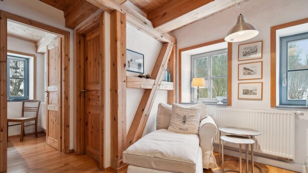 Quarto aconchegante com teto de madeira, cama com travesseiro, uma mesa pequena e janela com quadros na parede.