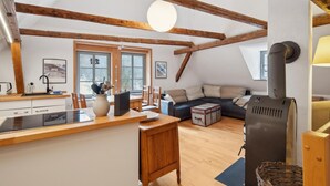 Um espaço de estar aconchegante em estilo loft, com vigas de madeira aparente, uma janela ampla, fogão embutido e um espaço de estar confortável.