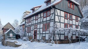Uma casa tradicional de enxaimel com telhado inclinado, rodeada por árvores cobertas de neve e um céu límpido.