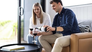 Deux personnes assises sur un canapé, avec une bouteille de vin et un verre.