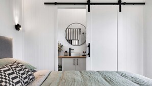 Une chambre à coucher comprenant un lit, une table de chevet, un miroir, une porte coulissante et un luminaire fixé au mur.