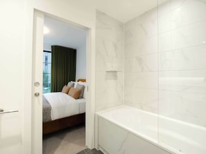 A hotel room with a bed, a bathroom with a bathtub, and a view of a building outside.