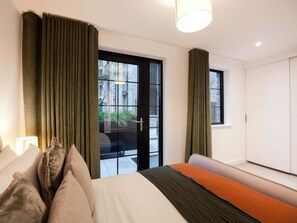 Ein modernes Schlafzimmer mit Bett, Vorhängen, einem Fenster und einer Tür zu einem Außenbereich.
