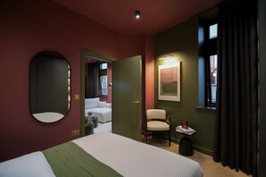 Et hotelværelse med seng, stol, lille bord, spejl, dør og et vindue med gardiner.