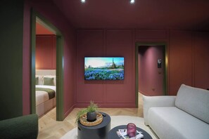 En moderne stue med et fladskærms-tv, en sofa, et sofabord og en seng i det tilstødende rum.