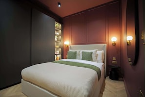 Een keurig opgemaakte hotelkamer met een groot bed, bedlampjes, een klein tafeltje en een spiegel.