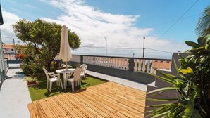 A wooden deck with a table and chairs, surrounded by greenery and a white fence.