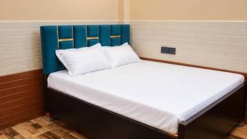 A hotel room with a bed, wooden flooring, a wall-mounted light, and a power outlet.