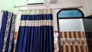 Ein Zimmer mit Deckenventilator, Klimaanlage, gemusterten Vorhängen und einem Fenster mit Metallgitter.